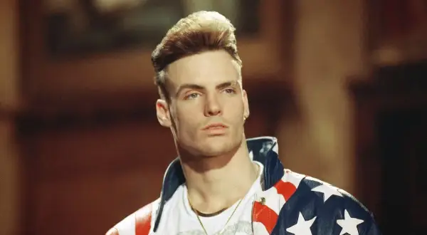 Homme blond avec une coiffure audacieuse, portant une veste aux couleurs du drapeau américain.