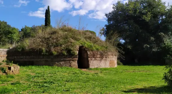 Antica tomba etrusca nel Lazio, con un ingresso ad arco e un tumulo ricoperto di vegetazione.