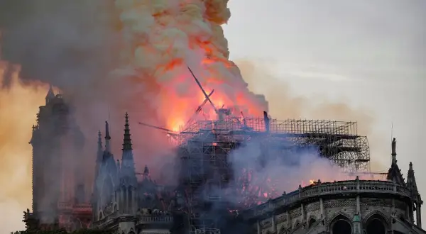 Notre Dame pożar: płomienie trawią dach katedry, unoszą się kłęby dymu. Widoczne rusztowania i zniszczona konstrukcja.