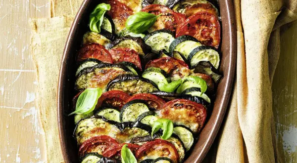 Gebackenes Gemüse aus Auberginen, Zucchini und Tomaten in einer Auflaufform, garniert mit Basilikum.
