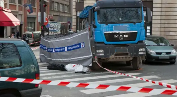 Scène d'accident avec camion bleu, voiture verte et ruban de sécurité. Un autocollant angle mort Europe est visible sur le camion.