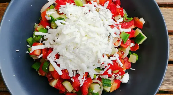En fräsch sopska salata med hackad tomat, gurka, paprika och lök, toppad med riven ost.