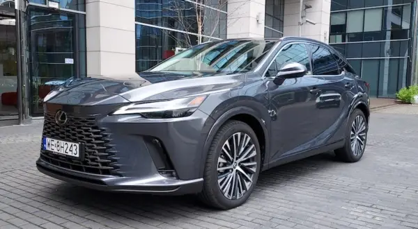 Elegancki, ciemnoszary Lexus RX 450h z nowoczesnym grillem i felgami stoi przed budynkiem biurowym.