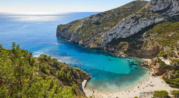 Bahía de aguas turquesas y arena dorada, rodeada de acantilados verdes. Un paraíso de playas bonitas con gente disfrutando del sol.