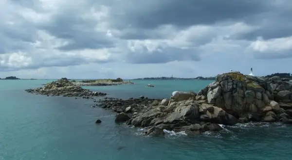 Îles rocheuses et mer turquoise près de Douarnenez, avec la Pointe du Raz en arrière-plan sous un ciel menaçant.