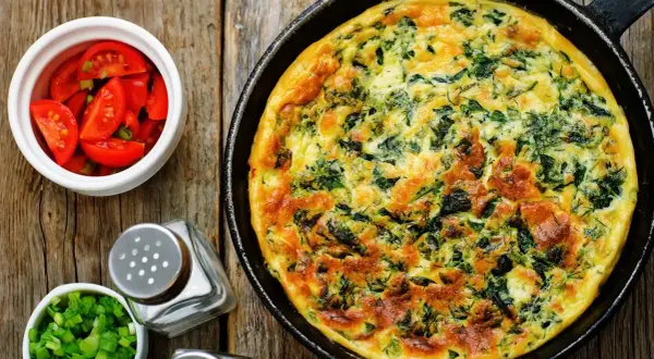 Frittata ze szpinakiem i serem, idealna jako pomysł, czym zastąpić węglowodany. Obok pomidorki i szczypiorek.