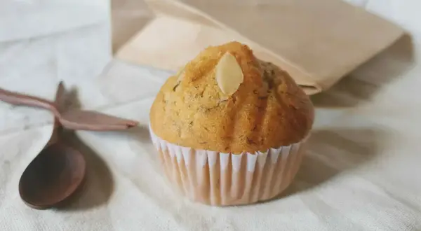 Un soffice muffin allo yogurt, guarnito con una mandorla, pronto per essere gustato con un cucchiaio di legno.
