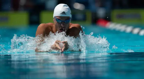 Swimmer executing perfect breaststroke technique, arms pulling water, creating a splash.