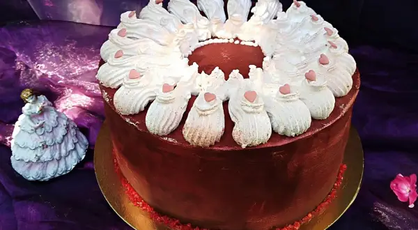 Elegancki tort w domu, ozdobiony bitą śmietaną i serduszkami. Obok stoi porcelanowa laleczka w sukni.