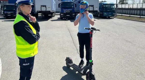 Policjantka sprawdza, czym można jeździć na kartę rowerową. Chłopiec zakłada kask na hulajnogę elektryczną.