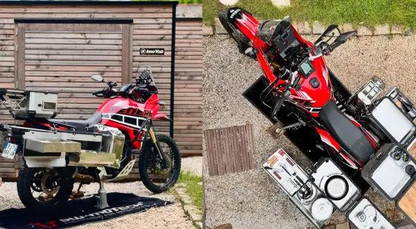 Una moto trail roja lista para la aventura, con maletas y equipo de camping.