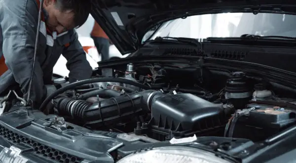 Mechanik w kombinezonie pracuje przy silniku samochodu, być może wykonując procedurę jak odpowietrzyć sprzęgło.