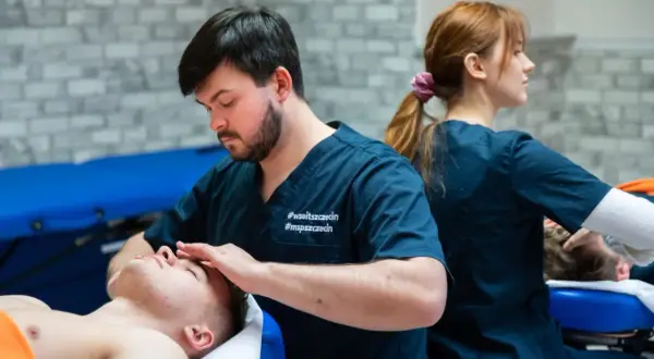 Fizjoterapeuta wykonuje masaż twarzy pacjentowi, w tle inna fizjoterapeutka.