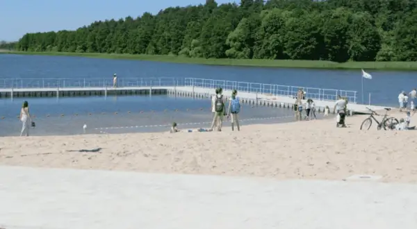 Słoneczne plaże na Mazurach przyciągają ludzi. Dzieci bawią się na piasku, a dorośli spacerują po pomoście.