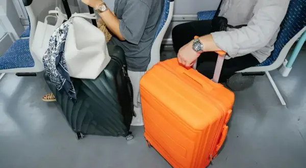 Podróżni z bagażem podręcznym: czarna walizka i jaskrawo pomarańczowa walizka stoją obok siebie w pociągu.