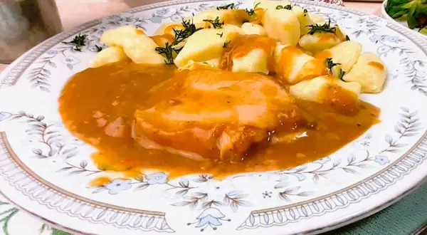 Pyszny schab w sosie, podany z kluskami śląskimi i posypany koperkiem. Danie prezentuje się apetycznie na ozdobnym talerzu.