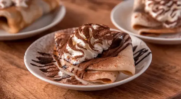 Deliziose crepes senza uova, guarnite con panna montata, cacao e sciroppo al cioccolato, un piacere per gli occhi e il palato.
