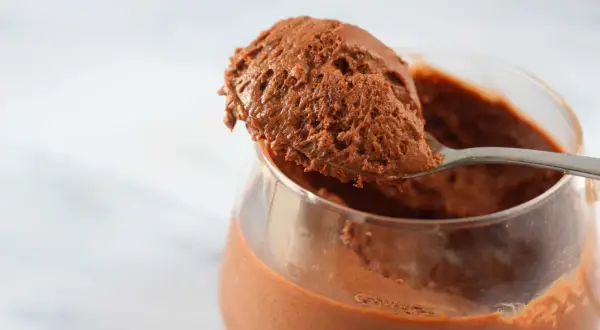 Un cucchiaio raccoglie una porzione generosa di soffice mousse al cioccolato da un bicchiere trasparente.