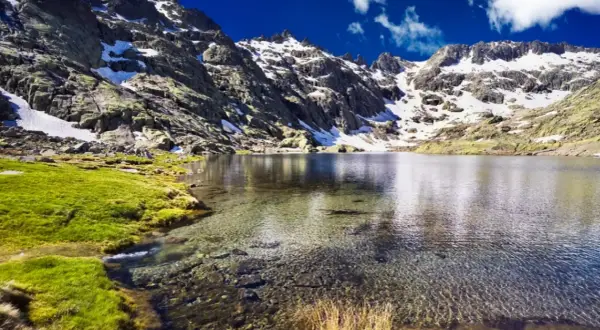 Espectacular vista de la ruta laguna grande de Gredos, con montañas nevadas, césped verde y aguas cristalinas.