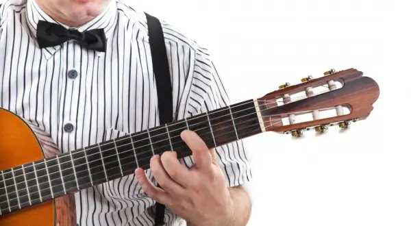Mężczyzna w muszce i koszuli w paski gra na gitarze, trzymając palce na gryfie. Widoczne są tabulatury na gitarę.