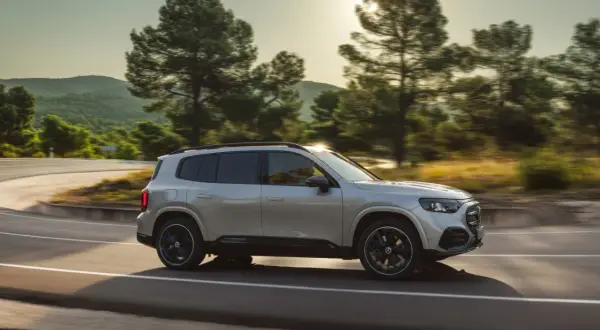 Nowy Mercedes GLB sunie po krętej drodze wśród drzew.