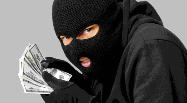 Un individu masqué, vêtu d'un sweat à capuche, compte des liasses de billets. Le vol a visiblement bien réussi.