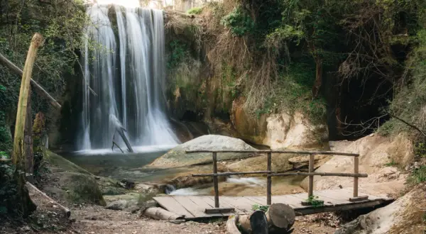 Cascata incantevole, le cascatelle di Sarnano creano un'atmosfera magica con la loro acqua impetuosa che scende tra rocce e vegetazione lussureggiante. Un piccolo ponte di legno invita all'esplorazione.