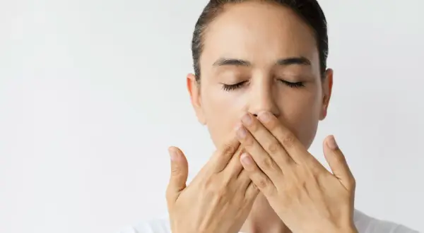 Donna con occhi chiusi copre la bocca con le mani, un'espressione che suggerisce una bocca amara o un segreto.