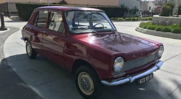 En röd Simca 1100 står parkerad på en solig uppfart.