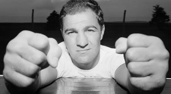 A determined boxer, perhaps a 49-0 legend, leans forward, fists clenched and ready.