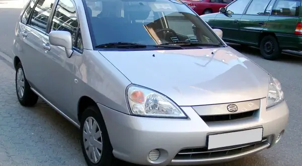 Srebrne Suzuki Liana stoi na ulicy, obok zielonego kombi.