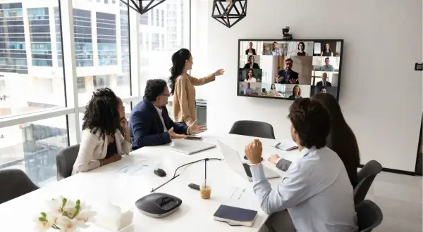 Ein Team im Büro nimmt an einer Videokonferenz teil, was zeigt, was ist hybrides arbeiten: Präsenz und Remote-Teilnehmer vereint.
