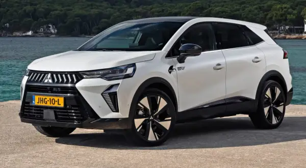 Nowy model Mitsubishi, biały SUV z czarnym dachem, stoi nad wodą. Nowoczesne linie i felgi podkreślają jego dynamiczny charakter.