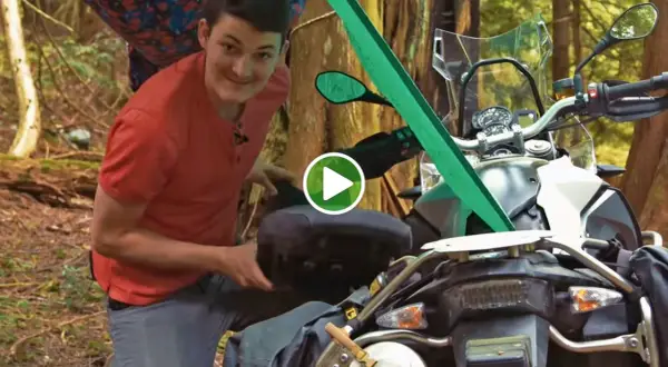 Mężczyzna przygotowuje motocykl do moto campingu w lesie, pakując bagaż.