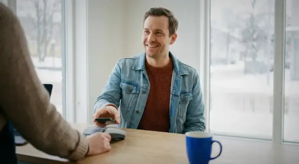 Uśmiechnięty mężczyzna płaci telefonem w Szwecji. Choć gotówka jest rzadkością, nadal można nią płacić.