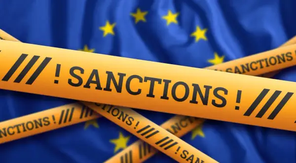 Żółte taśmy z napisem "SANCTIONS!" przecinają flagę Unii Europejskiej, symbolizując nałożone sankcje.