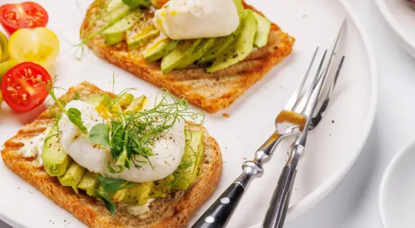 Zwei Scheiben Toast mit Avocado und pochiertem Ei, garniert mit Sprossen. Ein köstliches Egg Benedict Avocado Gericht.