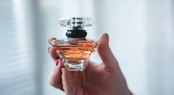Dłoń trzyma flakonik perfum o bursztynowym kolorze. Wygląda jak dzieło sztuki, może to baccarat kurkdjian?
