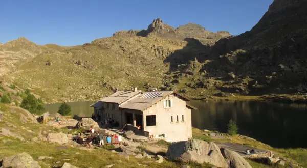 Refuge de montagne au bord d'un lac, idéal pour une randonnée vallée des merveilles 2 jours. Des randonneurs se reposent.