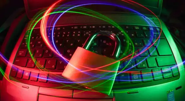 Kłódka na klawiaturze laptopa, otoczona kolorowymi światłami, symbolizuje bezpieczeństwo i ochronę, jak dobry antywirus na Linuxa.