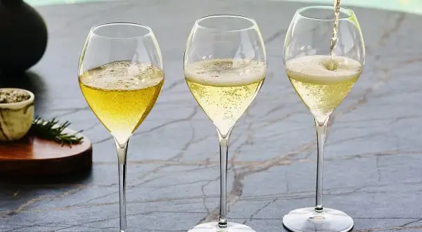 Trzy kieliszki wypełnione musującym winem. Jedno z nich jest nalewane z butelki. To jest właśnie cava!