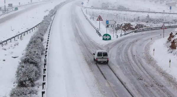 Nieve en la sierra de Madrid hoy. Una furgoneta blanca circula por una carretera nevada, con señales de tráfico y vegetación cubierta de blanco.