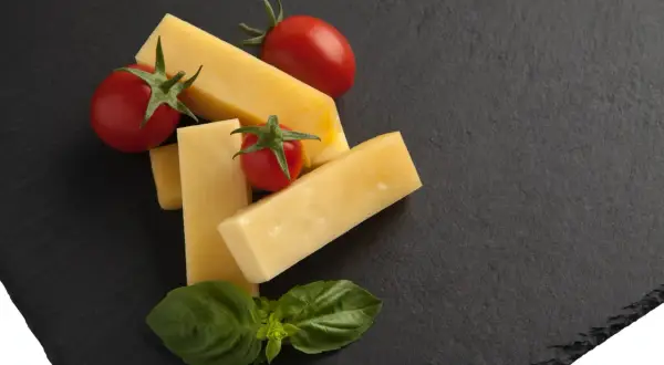 Kawałki żółtego sera, pomidorki koktajlowe i listki bazylii na czarnej desce. Czy to pecorino?