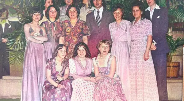 Grupa osób w eleganckich, pastelowych kreacjach. Widać długie suknie i garnitury, typowe dla lat 60 stylizacje.