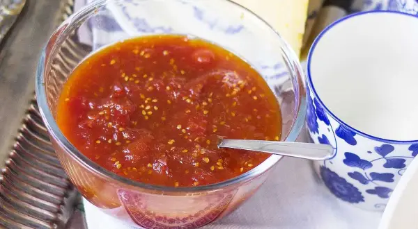 En skål med tomatmarmelad, perfekt för ett enkelt tomatmarmelad recept. Serveras med en sked och en blåvit kopp.