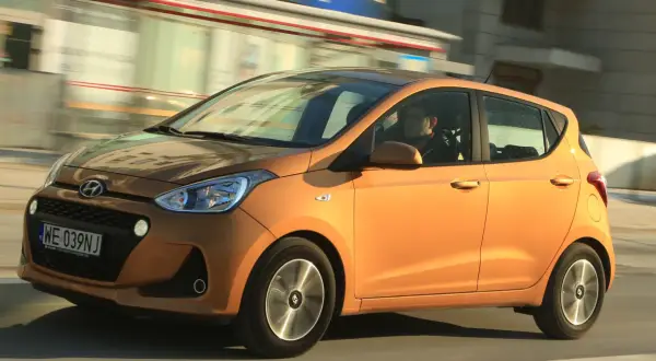 Pomarańczowy Hyundai i10 z kierowcą w środku jedzie ulicą.