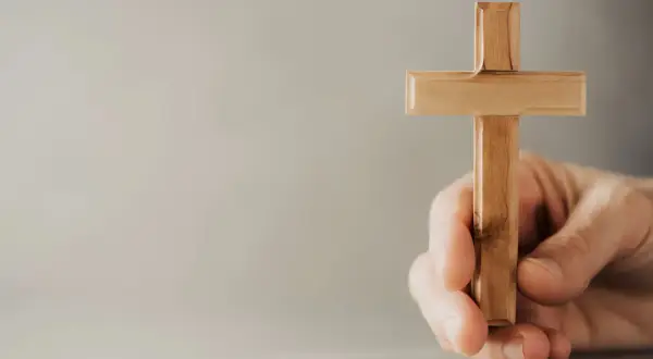 Eine Hand hält ein hölzernes Kreuz, ein Symbol, das Christen weltweit verbindet.