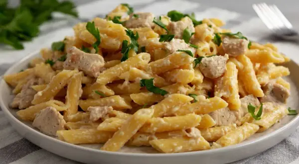 Penne con pollo w kremowym sosie, posypane świeżą natką pietruszki. Pyszne danie gotowe do podania.