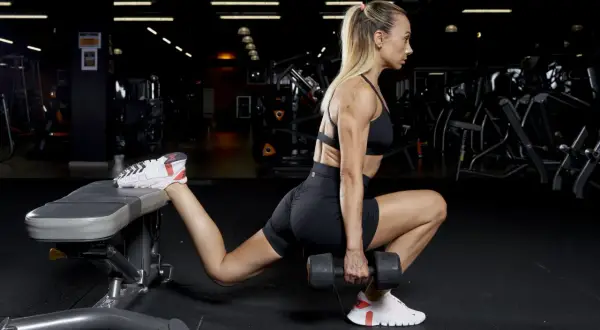 Donna esegue affondi bulgari con manubrio, concentrandosi sull'allenamento dei glutei e sull'iperestensione.