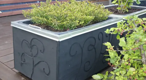 Svart blomlåda med dekorativa snirkar, perfekt för att bygga en murarbalja med grönska.